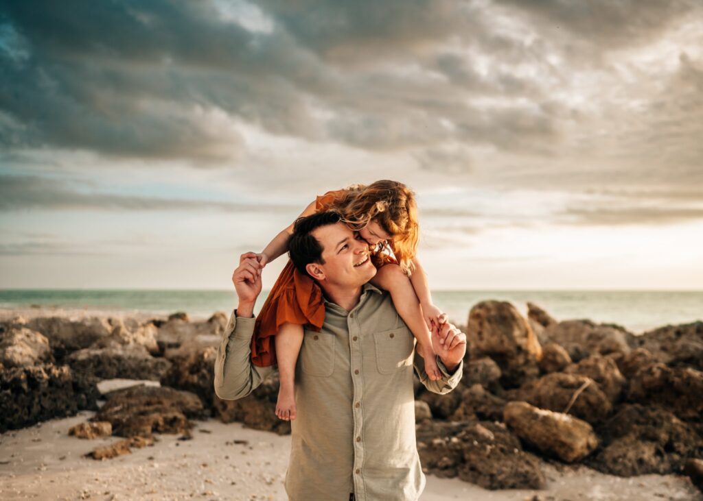 Dad-holding-daughter-on-beach-during-photoshoot-with-chasing-creative